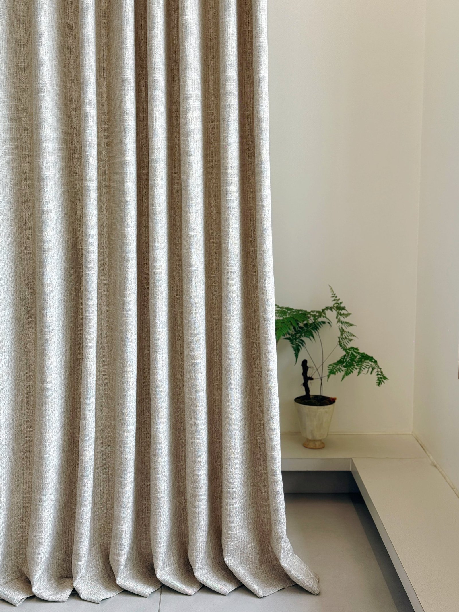Neutral curtain fabric falling in soft vertical folds beside a small plant